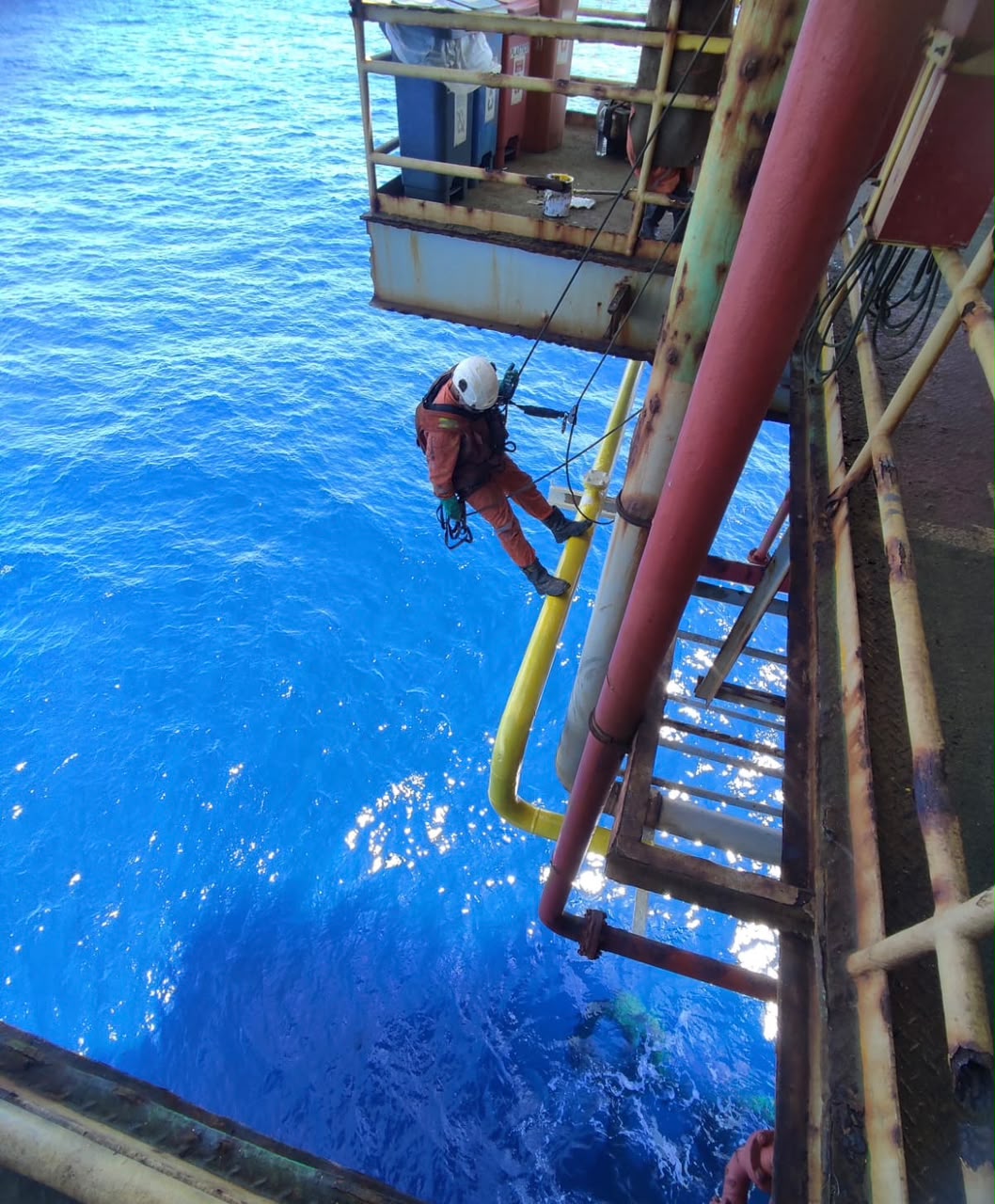 Técnico suspenso sobre o mar intervindo em tubulação de plataforma